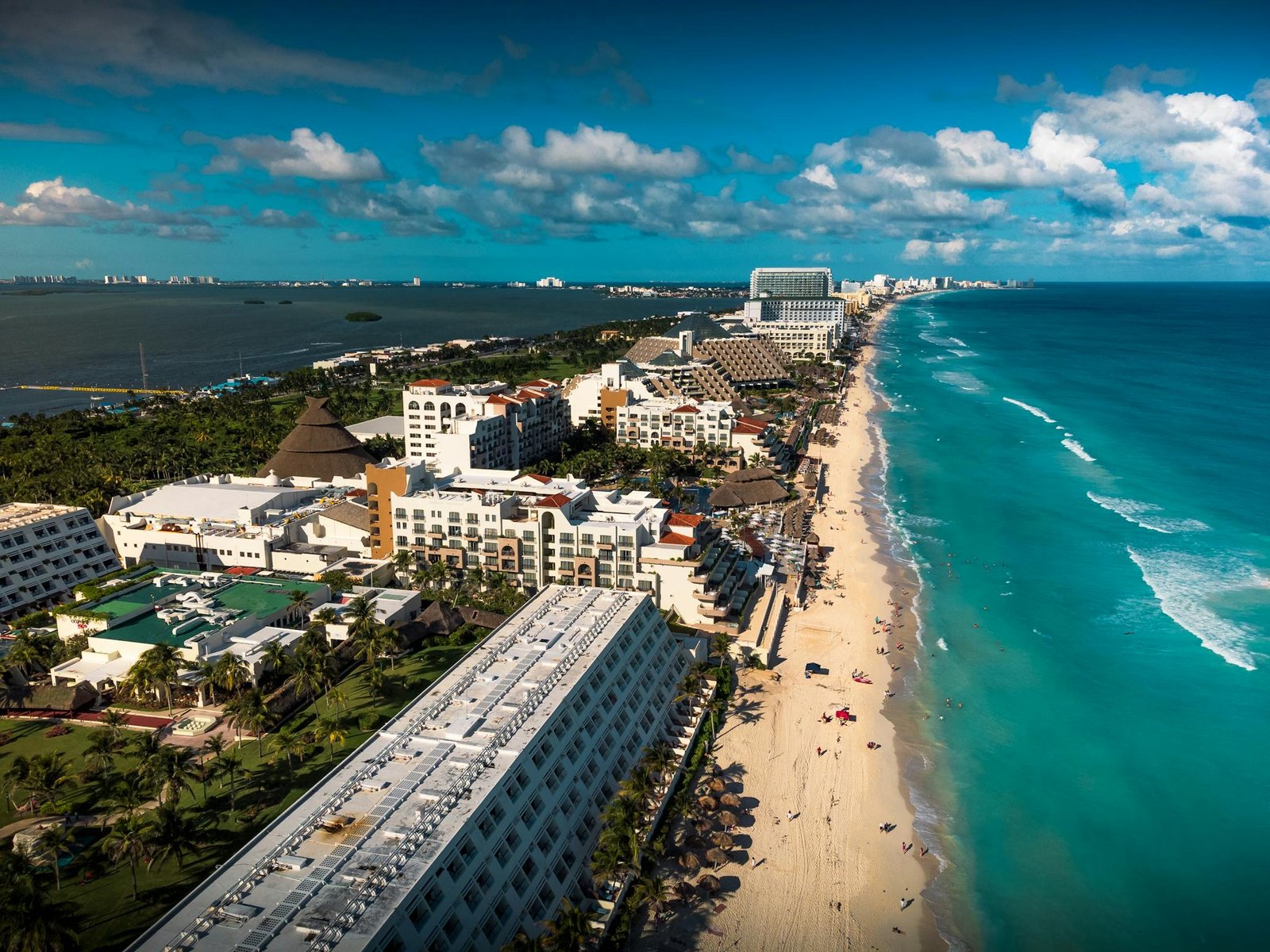 Stunning aerial view of Cancun, showcasing the vibrant beachfront, turquoise sea, and modern resorts under a bright blue sky.